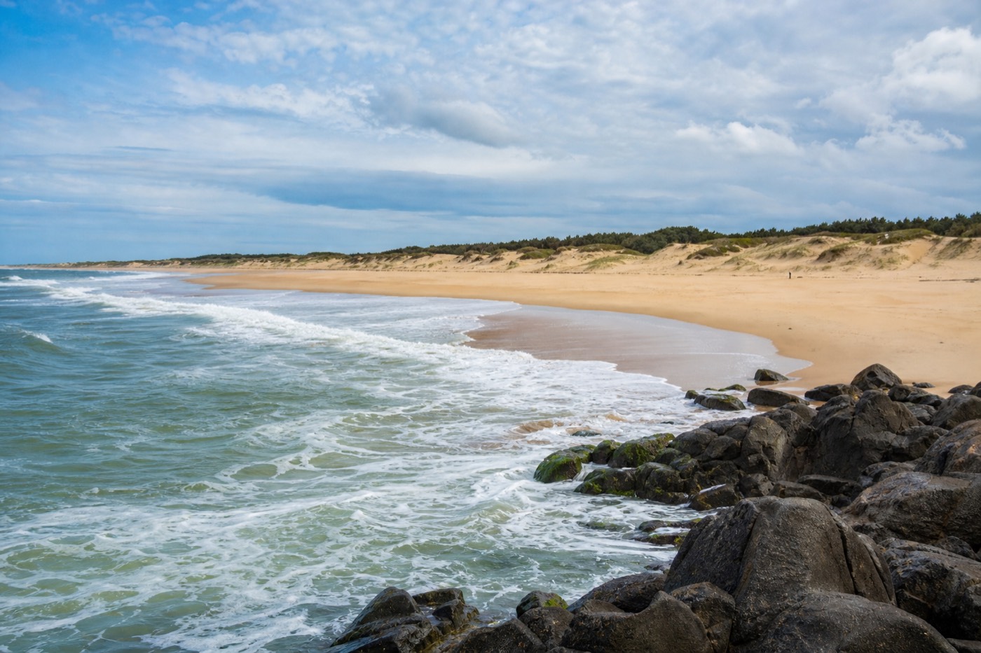 Wide sandy beach on the Punta del Este peninsula with Atlantic breakers rolling in on one side and calm sheltered water visible beyond the headland