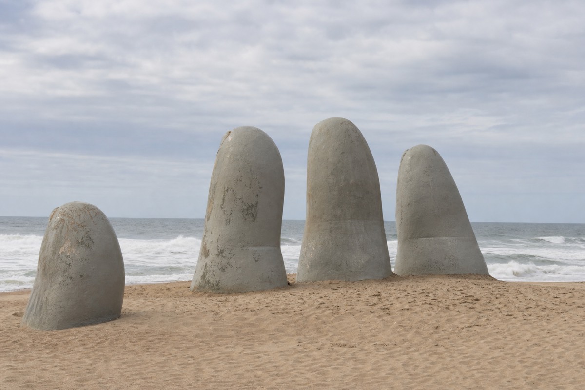 The giant concrete fingers of La Mano rising from the sand on Playa Brava with Atlantic surf breaking behind them at low sun