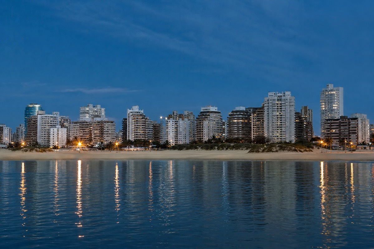 Wide view along the Punta del Este peninsula at dusk with apartment towers, the marina and the sheltered Playa Mansa shoreline curving away